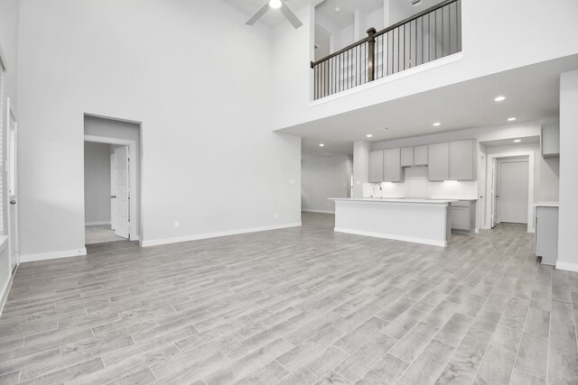 unfurnished living room featuring a towering ceiling, light hardwood / wood-style flooring, and ceiling fan