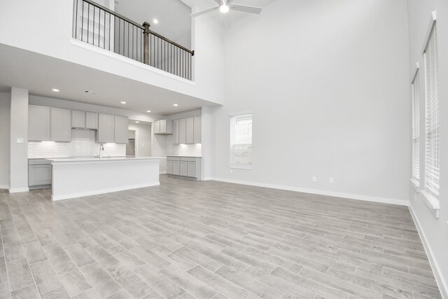 unfurnished living room featuring a towering ceiling, ceiling fan, sink, and light hardwood / wood-style floors