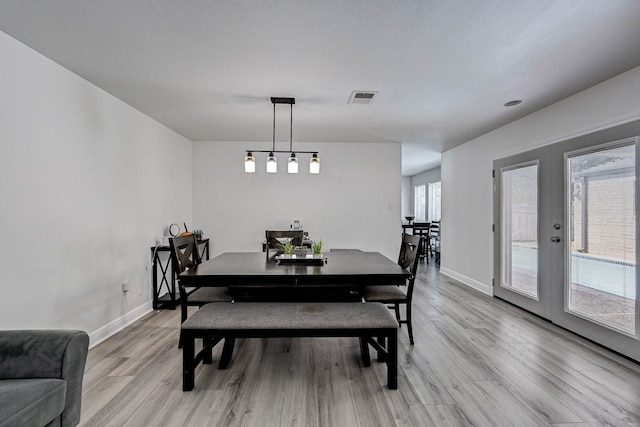 dining space with a wealth of natural light, french doors, and light hardwood / wood-style flooring