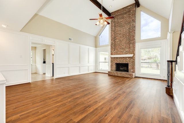 unfurnished living room featuring hardwood / wood-style floors, ceiling fan, high vaulted ceiling, a brick fireplace, and beamed ceiling