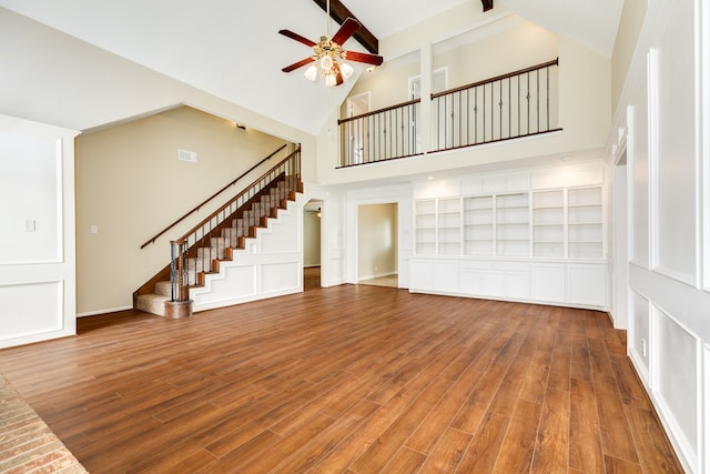 unfurnished living room featuring hardwood / wood-style flooring, high vaulted ceiling, built in shelves, and ceiling fan