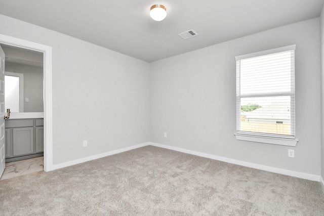 unfurnished bedroom with baseboards, visible vents, light carpet, and connected bathroom