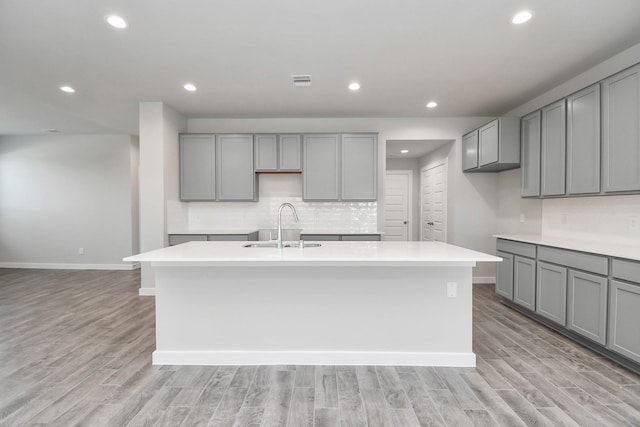 kitchen with a kitchen island with sink, a sink, gray cabinets, tasteful backsplash, and baseboards
