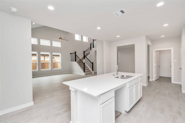 kitchen with sink, light wood-type flooring, white cabinetry, ceiling fan, and a center island with sink