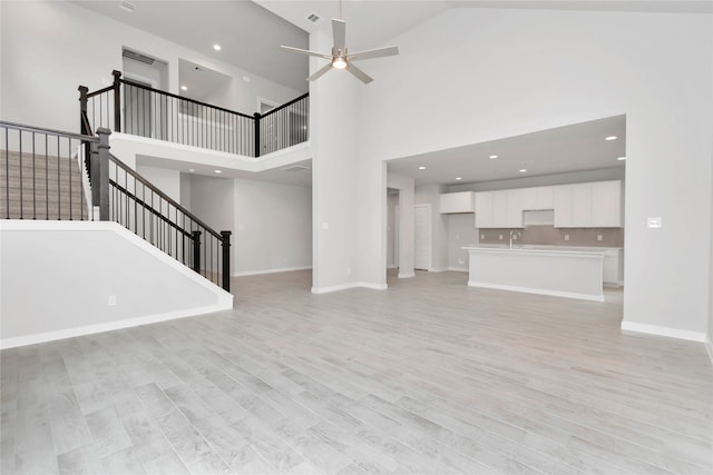 unfurnished living room featuring ceiling fan, a towering ceiling, sink, and light wood-type flooring