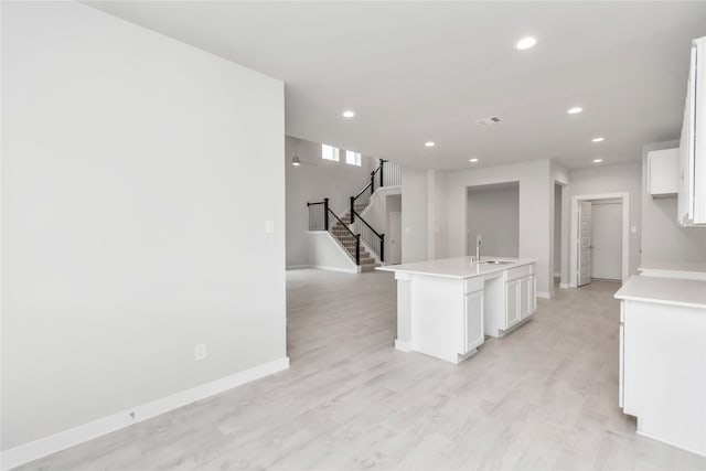 kitchen with light hardwood / wood-style flooring, white cabinets, a kitchen island with sink, and sink