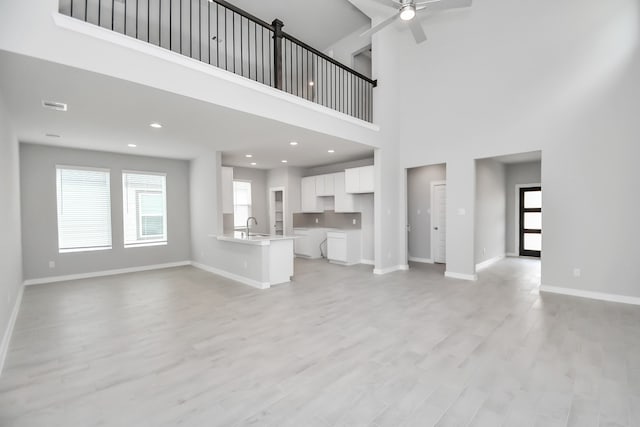 unfurnished living room featuring light hardwood / wood-style floors, a high ceiling, and ceiling fan