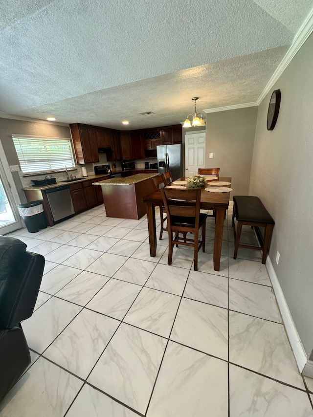 kitchen with appliances with stainless steel finishes, a textured ceiling, a center island, pendant lighting, and ornamental molding