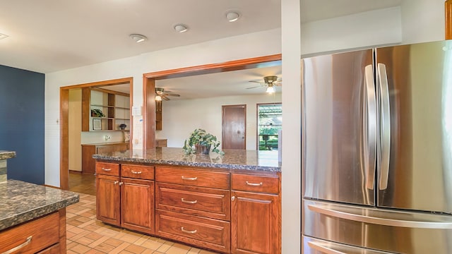 kitchen with dark stone countertops, ceiling fan, and stainless steel refrigerator