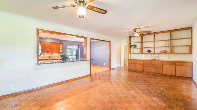 kitchen featuring kitchen peninsula, backsplash, dark stone countertops, light parquet floors, and ceiling fan