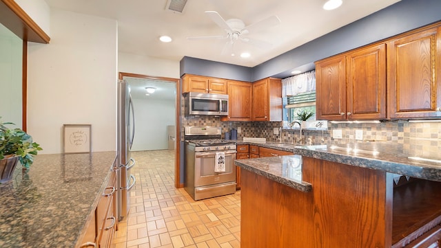 kitchen with tasteful backsplash, appliances with stainless steel finishes, sink, ceiling fan, and dark stone counters