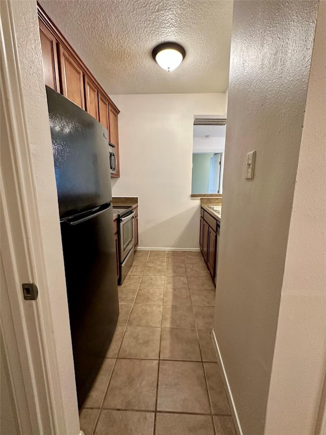 7029 N Holiday Dr, Galveston, TX 77550 - kitchen featuring light tile patterned floors, a textured ceiling, appliances with stainless steel finishes, baseboards, and brown cabinetry