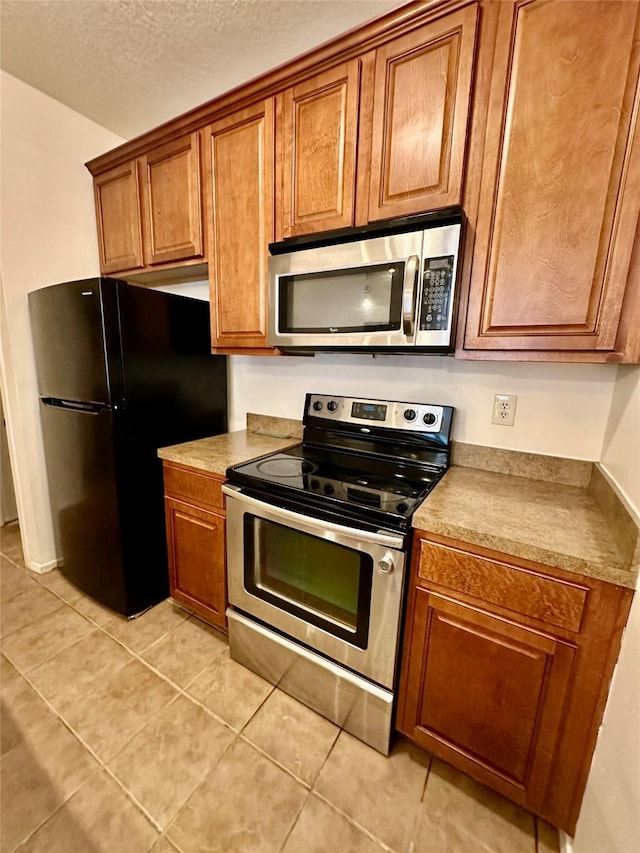 7029 N Holiday Dr, Galveston, TX 77550 - kitchen with light tile patterned floors, a textured ceiling, brown cabinets, and appliances with stainless steel finishes