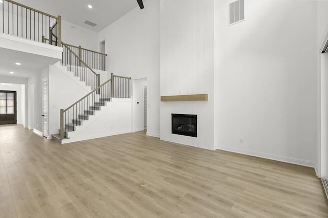 4622 Sycamore Way Rd, Fulshear, TX 77441 - unfurnished living room featuring a towering ceiling, stairway, light wood finished floors, a fireplace, and recessed lighting