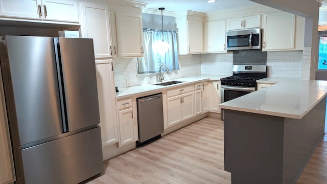 kitchen with white cabinets, hanging light fixtures, sink, appliances with stainless steel finishes, and light hardwood / wood-style floors