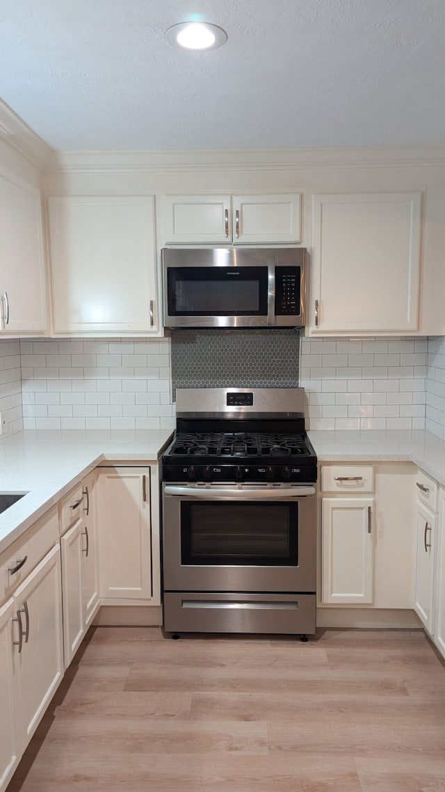 kitchen featuring white cabinets, light wood-type flooring, appliances with stainless steel finishes, and tasteful backsplash