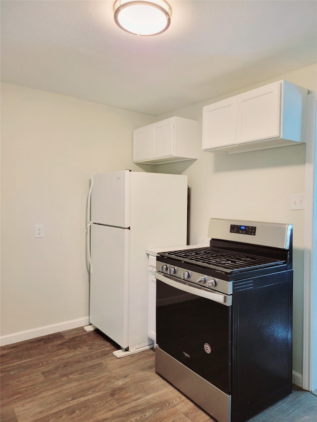 kitchen with dark wood-type flooring, stainless steel range with gas cooktop, white refrigerator, and white cabinets