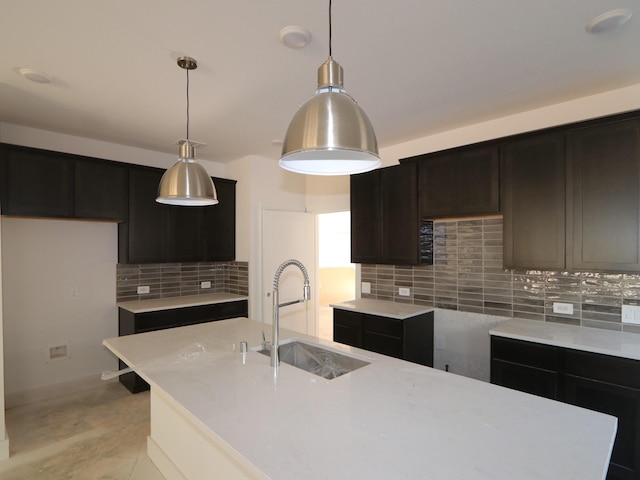 kitchen featuring pendant lighting, sink, backsplash, light stone counters, and a center island with sink