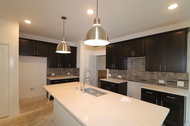 kitchen with sink, decorative light fixtures, light hardwood / wood-style flooring, a center island with sink, and backsplash