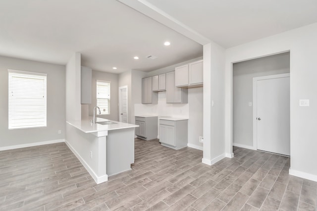 kitchen featuring light hardwood / wood-style flooring, gray cabinetry, sink, and kitchen peninsula