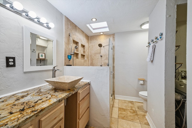 bathroom with vanity, toilet, a skylight, and tiled shower