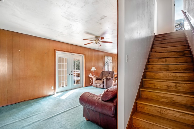 stairway featuring french doors, carpet, wooden walls, and ceiling fan