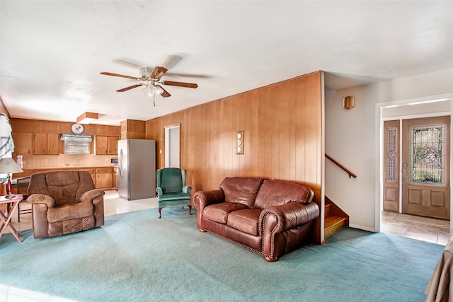 carpeted living room with ceiling fan and wood walls