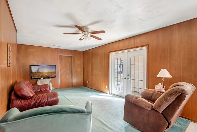 carpeted living room with french doors, wooden walls, and ceiling fan