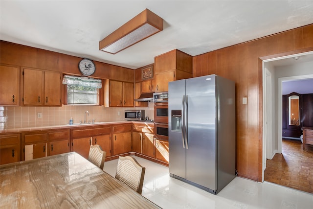 kitchen with decorative backsplash, sink, light parquet floors, appliances with stainless steel finishes, and wood walls