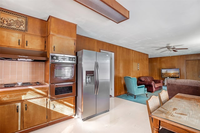 kitchen with backsplash, appliances with stainless steel finishes, wooden walls, and ceiling fan