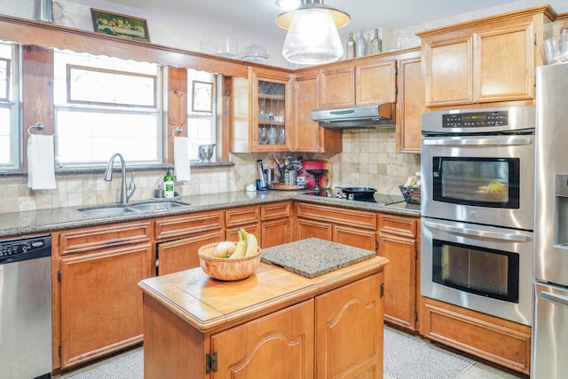 kitchen with light stone counters, backsplash, appliances with stainless steel finishes, a kitchen island, and sink