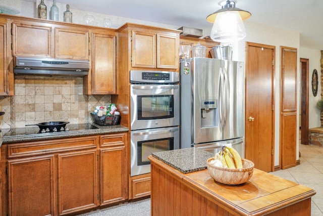 kitchen with backsplash, dark stone countertops, light tile patterned flooring, stainless steel appliances, and a center island