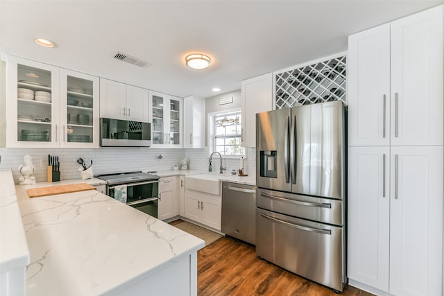 kitchen with light stone countertops, dark hardwood / wood-style floors, backsplash, white cabinets, and appliances with stainless steel finishes