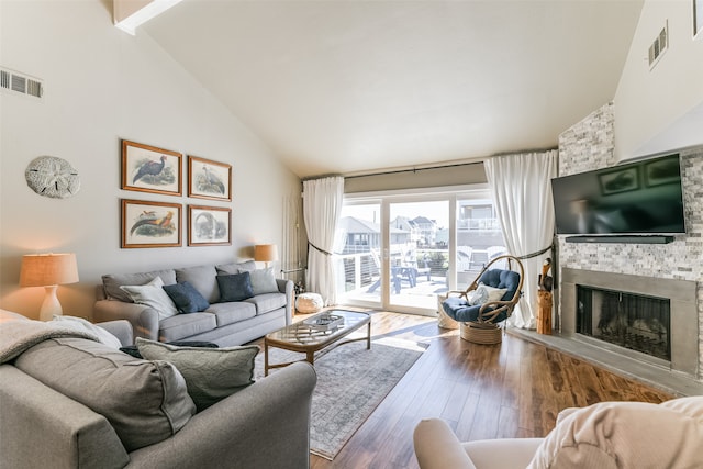 living room featuring wood-type flooring, high vaulted ceiling, and a stone fireplace