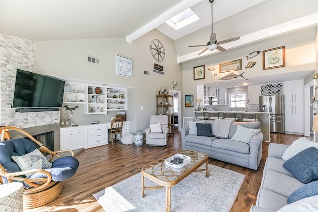 living room with beam ceiling, ceiling fan, a stone fireplace, high vaulted ceiling, and dark hardwood / wood-style floors