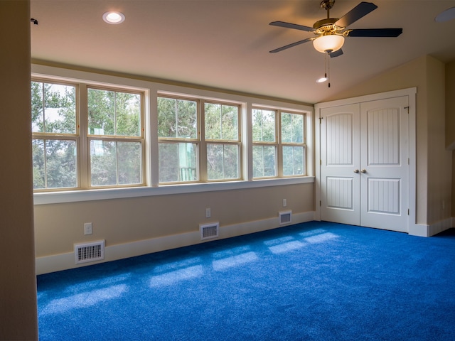 unfurnished bedroom featuring ceiling fan, lofted ceiling, multiple windows, and dark colored carpet