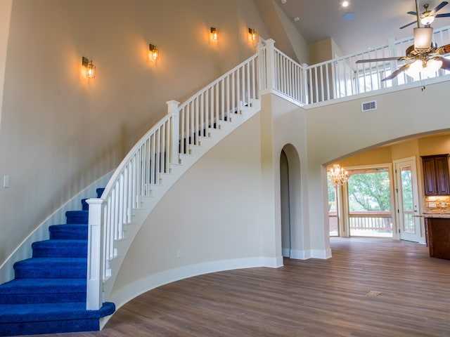 staircase featuring a towering ceiling, hardwood / wood-style flooring, and ceiling fan with notable chandelier