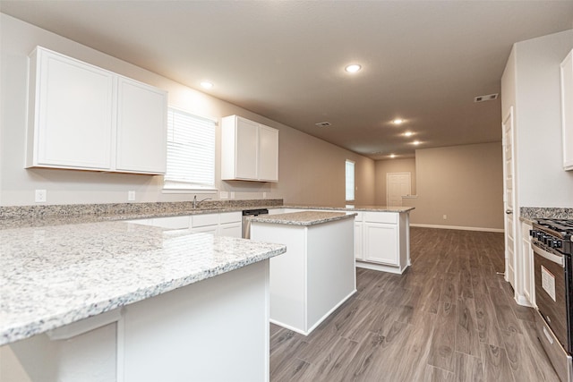 kitchen featuring white cabinetry, stainless steel gas stove, a center island, light stone counters, and hardwood / wood-style floors