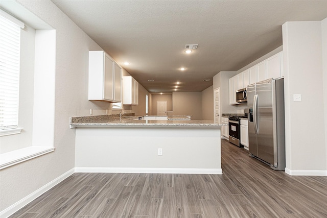 kitchen with kitchen peninsula, appliances with stainless steel finishes, hardwood / wood-style flooring, and white cabinetry