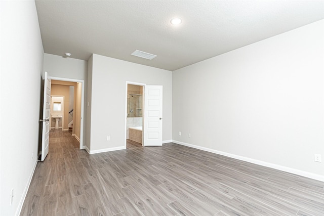 unfurnished bedroom featuring ensuite bath, a textured ceiling, and light wood-type flooring