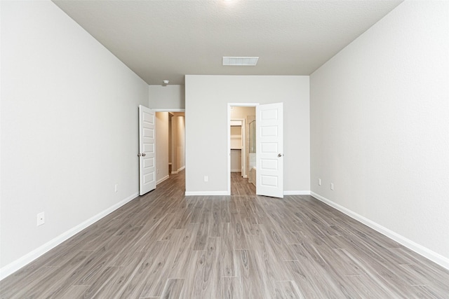 unfurnished bedroom with a textured ceiling, a walk in closet, and light hardwood / wood-style flooring