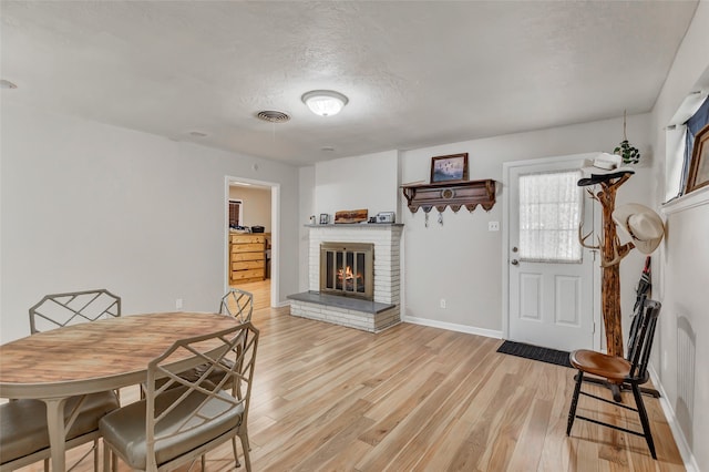 dining space with light hardwood / wood-style floors, a textured ceiling, and a fireplace