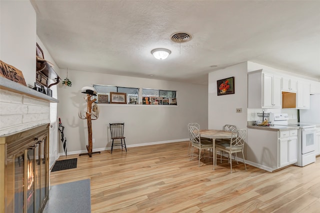 kitchen featuring white range with electric stovetop, white cabinetry, a stone fireplace, and light hardwood / wood-style flooring