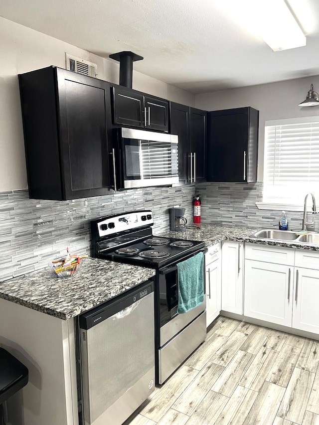 kitchen featuring white cabinets, tasteful backsplash, appliances with stainless steel finishes, light wood-type flooring, and sink