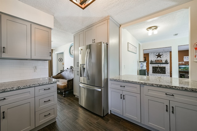 kitchen featuring gray cabinetry, light stone countertops, a textured ceiling, dark wood-type flooring, and stainless steel fridge with ice dispenser