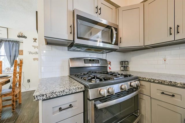 kitchen featuring dark wood-type flooring, light stone countertops, appliances with stainless steel finishes, and decorative backsplash