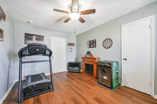 workout area with hardwood / wood-style floors, a textured ceiling, a fireplace, and ceiling fan