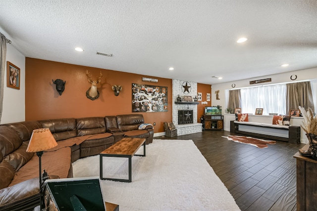 living room featuring dark wood-type flooring, a stone fireplace, and a textured ceiling