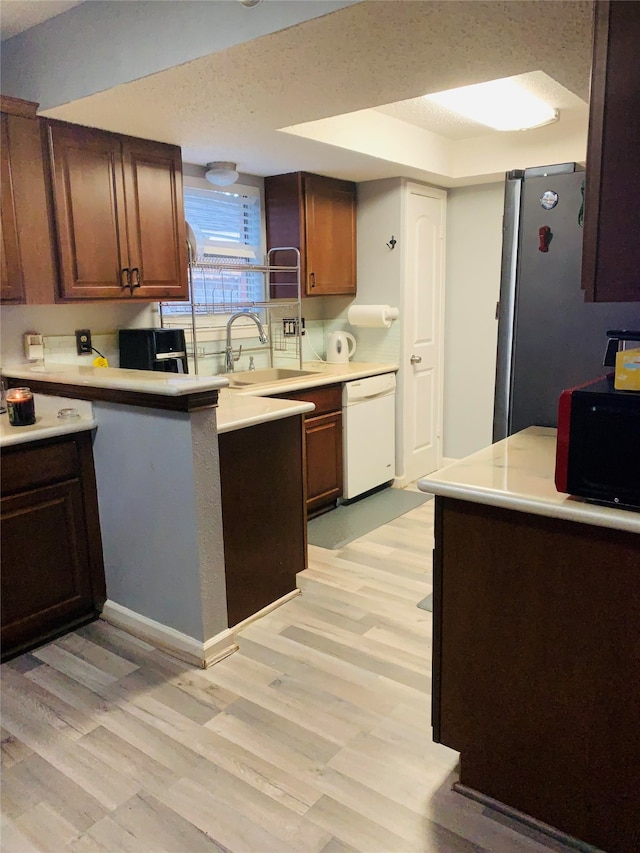 kitchen featuring dishwasher, kitchen peninsula, sink, light hardwood / wood-style floors, and stainless steel refrigerator