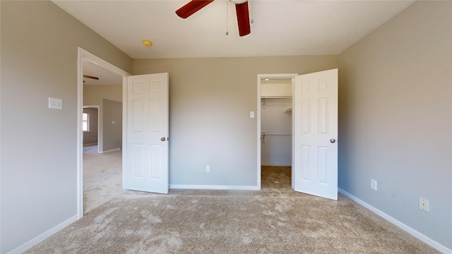 unfurnished bedroom featuring a spacious closet, light carpet, a closet, and ceiling fan